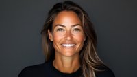 Confident mixed race woman with radiant smile and flowing brown hair against dark background, showcasing natural beauty and positive energy for wellness and lifestyle content.