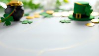 St. Patrick's Day festive background with leprechaun hat, pot of gold, shamrock leaves and coins on white surface for holiday celebration design.
