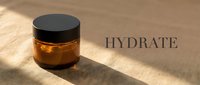 Amber glass jar with black lid containing golden skincare serum or oil on wooden surface with sunlight and hydrate text for cosmetic packaging and beauty product marketing.