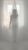 Woman with long hair standing behind sheer white curtains in bright natural light, creating ethereal silhouette effect for editorial, fashion, and artistic projects.