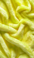 Soft yellow plush fabric with gentle folds and waves creating abstract texture pattern. Luxurious furry textile surface photographed in macro view.
