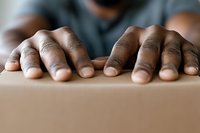 Close-up of African American male hands gripping cardboard box edge during moving or delivery process. Professional packaging and shipping concept.
