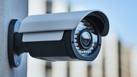 Modern security surveillance camera mounted on wall with infrared LED lights, black protective housing and adjustable bracket for monitoring and safety systems.
