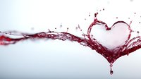 Red wine splash forming heart shape with droplets and dynamic motion against white background for romantic designs and beverage marketing campaigns.