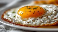 Golden fried egg with runny yolk and crispy edges seasoned with herbs on white plate, perfect for breakfast menu design and culinary content.