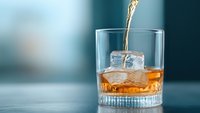 Golden whiskey splashing into crystal glass with ice cubes on turquoise background, capturing moment of pouring premium spirits in dramatic lighting.