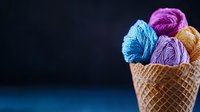 Colorful yarn balls arranged in waffle cone against dark background, creative knitting concept resembling ice cream scoops, artistic craft photography composition.