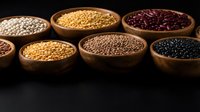 Assorted legumes and grains in wooden bowls including lentils, chickpeas, beans and seeds on dark background for cooking and nutrition content.