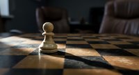 White chess pawn standing alone on wooden chessboard with dramatic lighting and blurred background creating strategic business concept atmosphere.