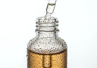 Clear glass dropper bottle with amber liquid inside, covered in water droplets showing freshness and purity for cosmetic or essential oil product use.