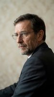 Distinguished mature Caucasian businessman with glasses and beard in formal suit looking thoughtfully over shoulder in professional portrait setting.