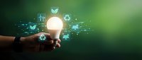 Glowing light bulb held by hand with green energy icons, symbolizing sustainable innovation, eco-friendly technology, and renewable energy concepts.