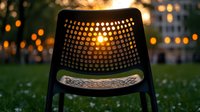 Modern outdoor chair with perforated backrest silhouetted against sunset bokeh lights in urban park setting, creating atmospheric evening ambiance.