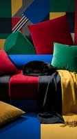 Black cat sleeping on colorful geometric patchwork sofa with vibrant cushions and throw blanket in modern living room interior design setting.