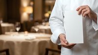 Waiter in white uniform holding empty tray in upscale restaurant dining room with elegant table setting and warm ambient lighting for hospitality service.