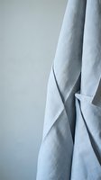 Soft blue linen fabric draped elegantly with natural folds and wrinkles creating organic texture patterns for interior design and textile backgrounds.
