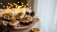 Festive holiday appetizers with smoked salmon and cream cheese on dark bread, garnished with fresh dill and served on elegant plate with warm bokeh lights.