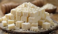 Fresh feta cheese cubes on rustic wooden board with crumbled cheese on top, macro food photography in natural light, dairy product closeup.