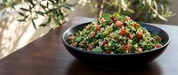 Tabbouleh salad with quinoa, fresh herbs, tomatoes and vegetables in black bowl on wooden table with natural sunlight for food photography and culinary content.