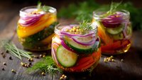 Fresh pickled vegetables in glass jars with dill, cucumber, red onion, carrot and spices on rustic wooden background. Homemade fermented food preservation.