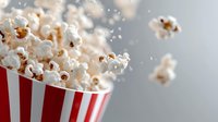 Fresh popcorn exploding from classic red and white striped container against gray background, capturing motion of kernels in mid-air for cinema and entertainment.