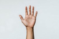 Open palm of a young person with medium skin tone showing five fingers raised against light background, representing greeting, voting, or participation gesture.