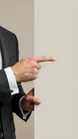 Businessman in dark suit pointing finger gesture showing direction or making presentation on neutral background for business communication concepts.