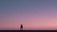 Romantic couple silhouette embracing against stunning purple pink sunset sky horizon creating intimate moment for love relationship concepts.