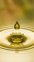 Golden water drop creating ripples and crown splash in liquid surface with warm yellow tones and soft bokeh background for wellness and purity concepts.