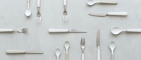 Overhead view of assorted silver flatware and cutlery arranged on neutral background, suitable for dining, restaurant, and tableware design projects.