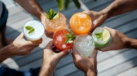 Diverse colorful cocktails with fresh mint and citrus garnish in hands toasting together, overhead view of summer drinks celebration gathering.