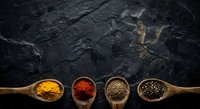 Colorful spices in wooden spoons arranged on dark slate background. Turmeric, paprika, coriander and peppercorns for cooking and seasoning culinary dishes.