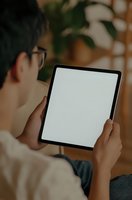 Asian male professional holding digital tablet with blank white screen in home office setting, mockup ready for product placement and digital content.