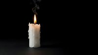 Burning white candle with melted wax drips and smoke against black background for meditation, relaxation, spa treatments, romantic atmosphere and home decor.