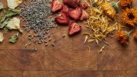 Assorted dried herbs, spices, flowers and seeds scattered on rustic wooden surface for natural cooking, aromatherapy and wellness applications.