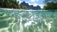 Underwater view of tropical lagoon with sunlight dancing on turquoise water surface, dramatic mountain silhouettes and palm trees visible above waterline.