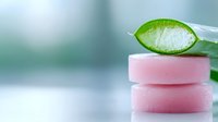 Fresh aloe vera leaf slice on stack of pink organic soap bars against soft blurred background, natural skincare and spa concept.