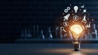Glowing light bulb with business innovation icons floating above including dollar signs, charts, and startup symbols representing creative entrepreneurship.