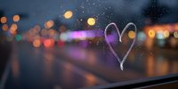 Heart drawn on foggy car window with colorful city lights bokeh background at night creating romantic atmosphere for love concepts.