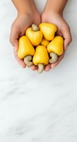 Hands holding fresh yellow cashew apples and cashew nuts on white marble background, promoting healthy organic produce and natural nutrition.
