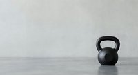 Black kettlebell on concrete floor against white wall in minimalist gym setting for fitness and strength training workouts.
