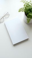 Clean white notebook with eyeglasses and green plant on minimalist desk setup for office workspace branding and productivity concepts.