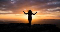 Woman silhouette with raised arms celebrating freedom on mountain peak at golden sunset with dramatic cloudy sky and scenic landscape view.