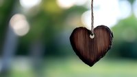 Rustic wooden heart decoration hanging on rope string against soft green bokeh background, creating romantic valentine or wedding atmosphere.