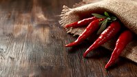 Fresh red chili peppers spilling from burlap sack onto rustic wooden surface, dramatic side lighting creates mood for food photography and restaurant menus.