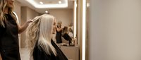 Professional hairstylist working on blonde client hair in modern salon with mirror lighting and styling chair for beauty services.
