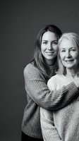 Young adult daughter embracing senior mother in cozy sweaters, black and white portrait showing intergenerational love and family bond for emotional campaigns.