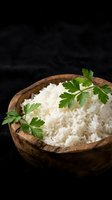 Cooked white rice in wooden bowl garnished with fresh parsley on dark background for culinary and cooking projects.
