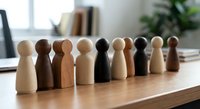 Diverse wooden peg people figures in various skin tones standing together on desk representing unity, inclusion, teamwork and multicultural diversity.