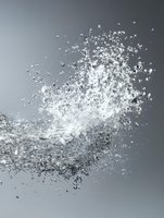 Dynamic splash of water droplets frozen in motion against gray background, creating dramatic explosion effect with crystalline particles suspended in air.